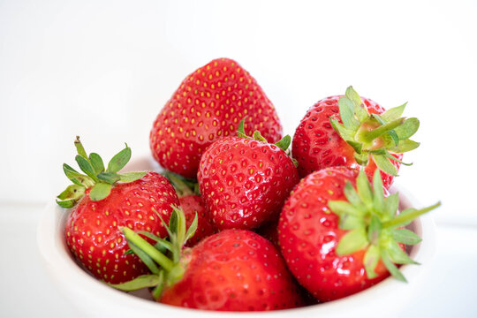 Close up macro image of vivid red strawberries with green stalks against a white background.  Complementary colour scheme with white negative space for copy text or customisation