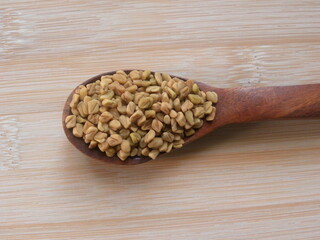 Yellow dry Fenugreek seeds on wooden spoon
