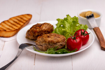 meatballs with vegetables on a white plate with a slice of toasted bread and mustard on a white wooden background