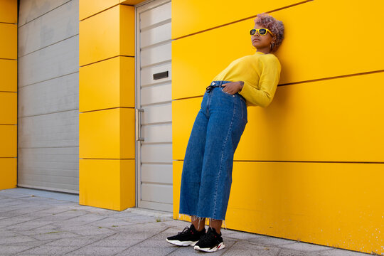 fashionable young girl leaning on yellow street wall