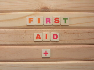Word First Aid with + symbol on wood background