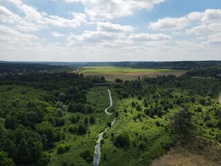 Aerial view of a river flowing through a summer landscape with trees and fields and blue sky with clouds
