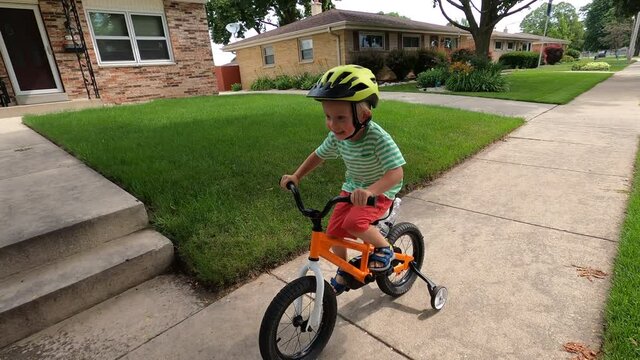 Child Is Riding A Bike On A Street Sidewalk In An American Neighborhood. Happy Childhood Memories Concept.  Daytime, Summer