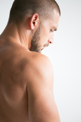 young man with neck pain. A man with a naked athletic torso poses in a photo studio on a white background. A healthy image of a strong, well-trained male body. Shows the muscles.