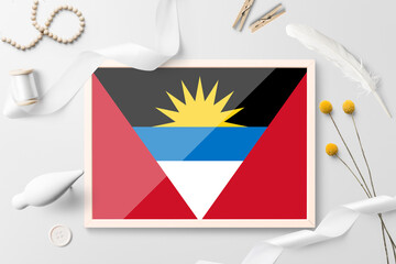 Antigua and Barbuda flag in wooden frame on white creative background. White theme, feather, daisy, button, ribbon objects.