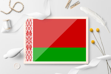 Belarus flag in wooden frame on white creative background. White theme, feather, daisy, button, ribbon objects.