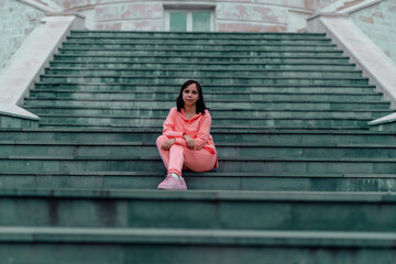 Fototapeta na wymiar Young woman poses on stairs of manor. Adult female sitting on steps of Palace.