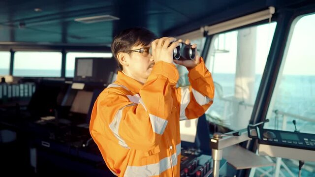Filipino deck Officer on bridge of vessel or ship wearing coverall. He is looking through binoculars. COLREG navigaton watch at sea