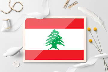 Lebanon flag in wooden frame on white creative background. White theme, feather, daisy, button,...