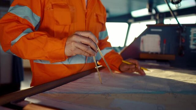 Filipino deck Officer on bridge of vessel or ship wearing coverall during navigaton watch at sea . He is plotting position on chart