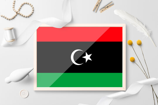 Libya flag in wooden frame on white creative background. White theme, feather, daisy, button, ribbon objects.