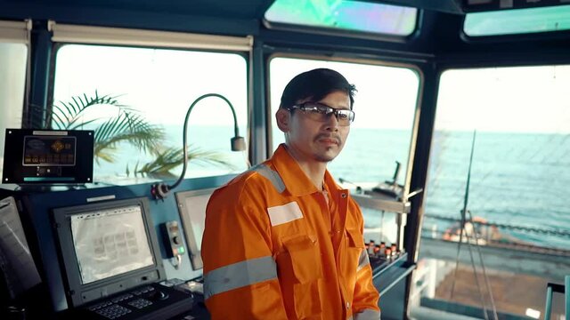 Filipino deck Officer on bridge of vessel or ship wearing coverall during navigaton watch at sea