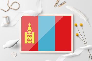 Mongolia flag in wooden frame on white creative background. White theme, feather, daisy, button, ribbon objects.