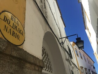 Surreal view of the ancient Imaginary Street -- Rua do Imaginario, &Eacute;vora, Portugal. Ancient yellow and white architecture along narrow, crooked street against blue sky. High quality photo in natural