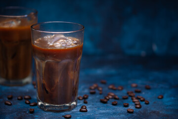 Cold summer drink, iced coffee with cream or milk.Cool drink with coffee grains on blue background