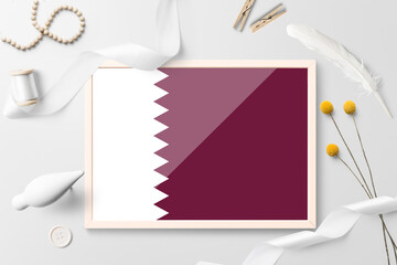 Qatar flag in wooden frame on white creative background. White theme, feather, daisy, button, ribbon objects.