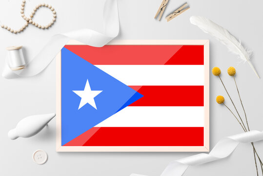 Puerto Rico flag in wooden frame on white creative background. White theme, feather, daisy, button, ribbon objects.
