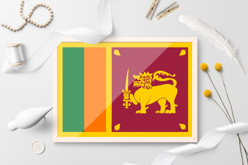 Sri Lanka flag in wooden frame on white creative background. White theme, feather, daisy, button, ribbon objects.