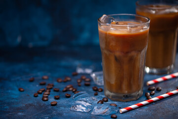Cold summer drink, iced coffee with cream or milk.Cool drink with coffee grains on blue background