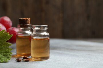 Bottles of natural grape seed oil on grey table, space for text. Organic cosmetic