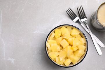 Tasty canned pineapple pieces and forks on light grey marble table, flat lay. Space for text
