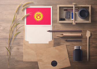 Kyrgyzstan invitation, celebration letter concept. Flag with craft paper and envelope. Retro theme with divide, ink, wooden pen objects.