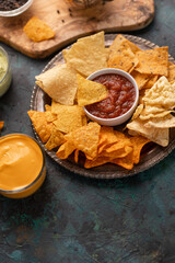 Snacks and chips with potatoes and pita chips, dip, and salsa, on a dark green background