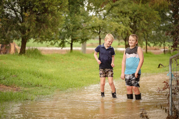 Obraz premium Two young brothers playing in flooded creek wearing gumboots in water