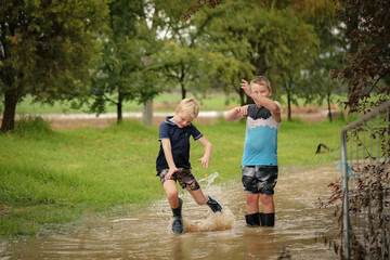 Two young brothers walking along flooded creek wearing gumboots in water