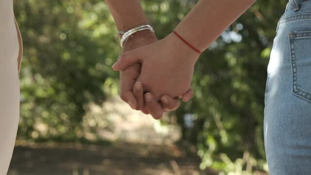 Young lesbian couple holding hands walking at sunset. Close up