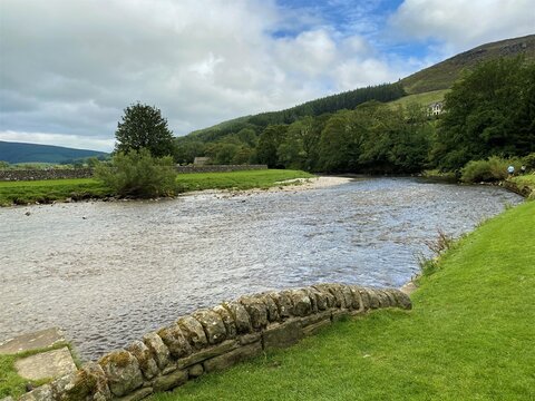 The river Wharfe, as it flows past the village of Burnsall, with trees and hills in the distance in, Burnsall, Skipton, UK © derek oldfield