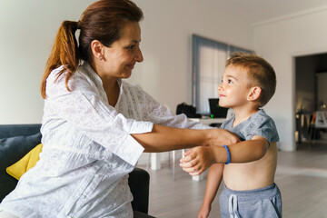 Adult woman help small child boy to get dressed at home - Caucasian Mother and 4 year old son putting on t-shirt in room - front view half length - growing up bonding care trust and support concept