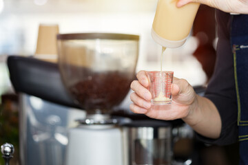 Barista's hand is pouring milk in a measuring cup.
