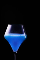 Blue drink is poured into a glass. Black background.