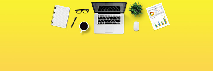 Top view business office desk with laptop, coffee, notebook, a report paper, and office supplies / Creative flat lay photo of workspace desk and copy space / Panoramic banner yellow background