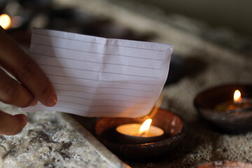 Hand holding a white lined paper note with personal secret prayer. Burn it on a burning candle in a...