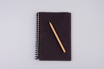 Top view of closed black cover notebook with pencil on white desk background