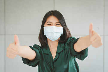 Happy woman wearing medical face mask showing thumb up