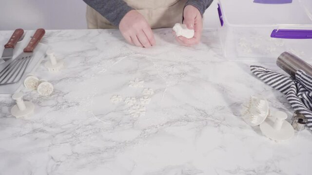 Step by step. Cutting out snowflakes with cookie cutters out of white fondant on a marble counter.