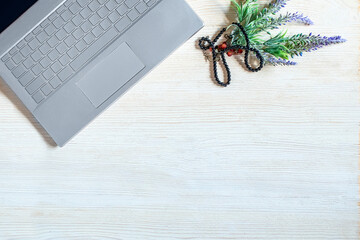 laptop for work, beads and flowers on a white wooden background