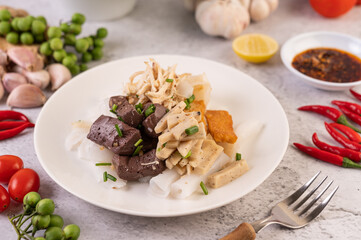Large noodle noodles with pork blood sausage, crispy pork slices, and sliced ​​onions in a white plate.