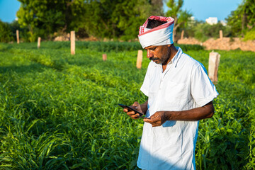 Mature Indian farmer holding a master credit debit card with mobile phone doing mobile internet...