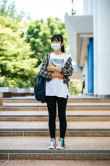 Obraz premium Female students wear masks, stand on stairs and hold books.