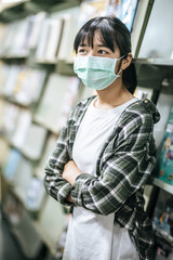A woman wearing a mask and searching for books in the library.