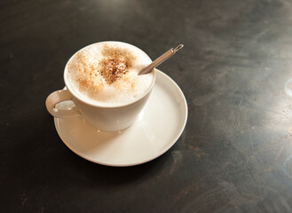 Small cup and saucer of expresso with cinnamon sprinkled on top and small whipping tool sticking...