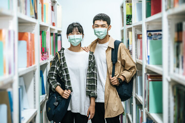 Men and women carrying a backpack and searching for books in the library.