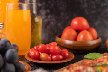 Fresh tomatoes in a wooden cup, grapes and orange juice in a glass.