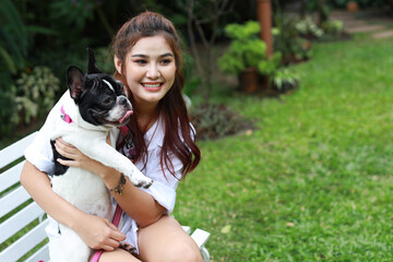 beautiful young asian woman wearing white shirt sitting on white bench and playing with cute dog with happy laughing face