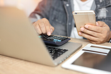 Man hands in grey jean sitting and using calculator and laptop computer on wooden table for online payment or shopping online. Business man using mobile phone while sitting. E-Banking concept