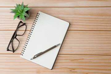 Top view of Notebooks, pens, glasses, cactus  on wooden desks with sunlight and copy space